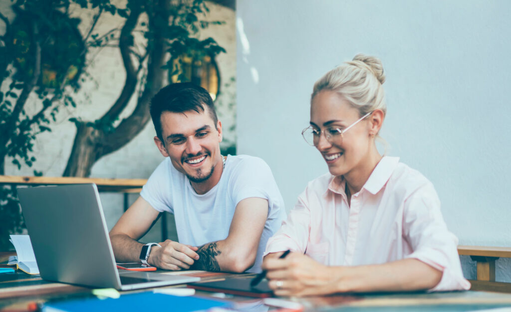 Modern happy young man and woman laughing while doing teamwork