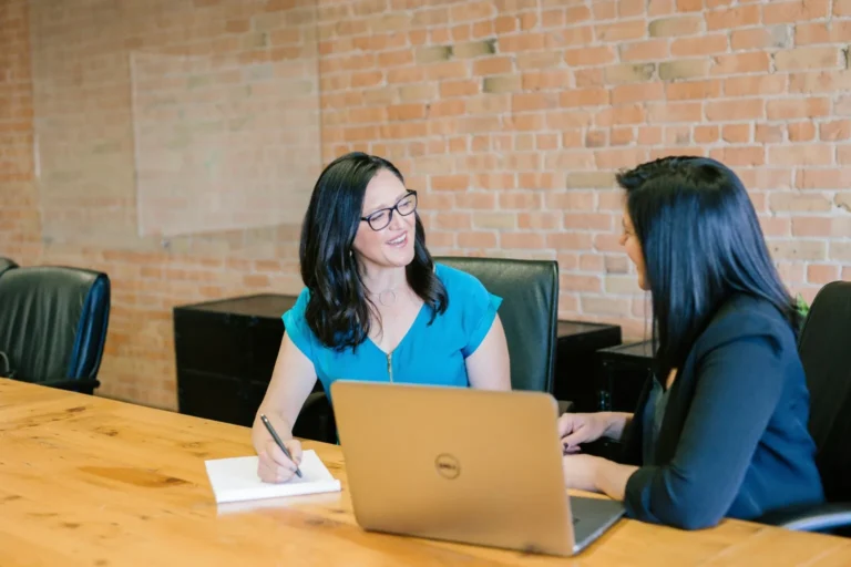 Two women sitting at a table discussing how to maintain an income statement.